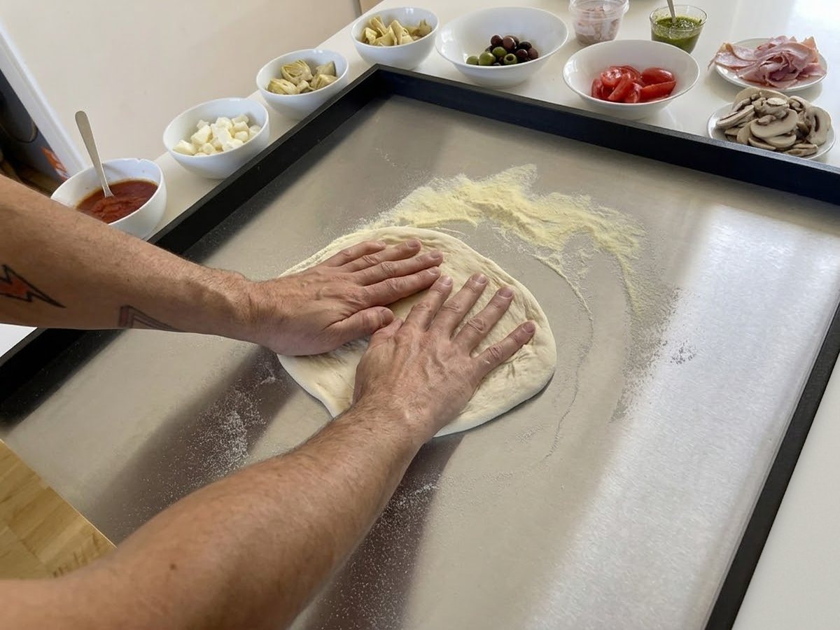Hands pressing out pizza dough on Stendì, with the low sides around the steel and the open front